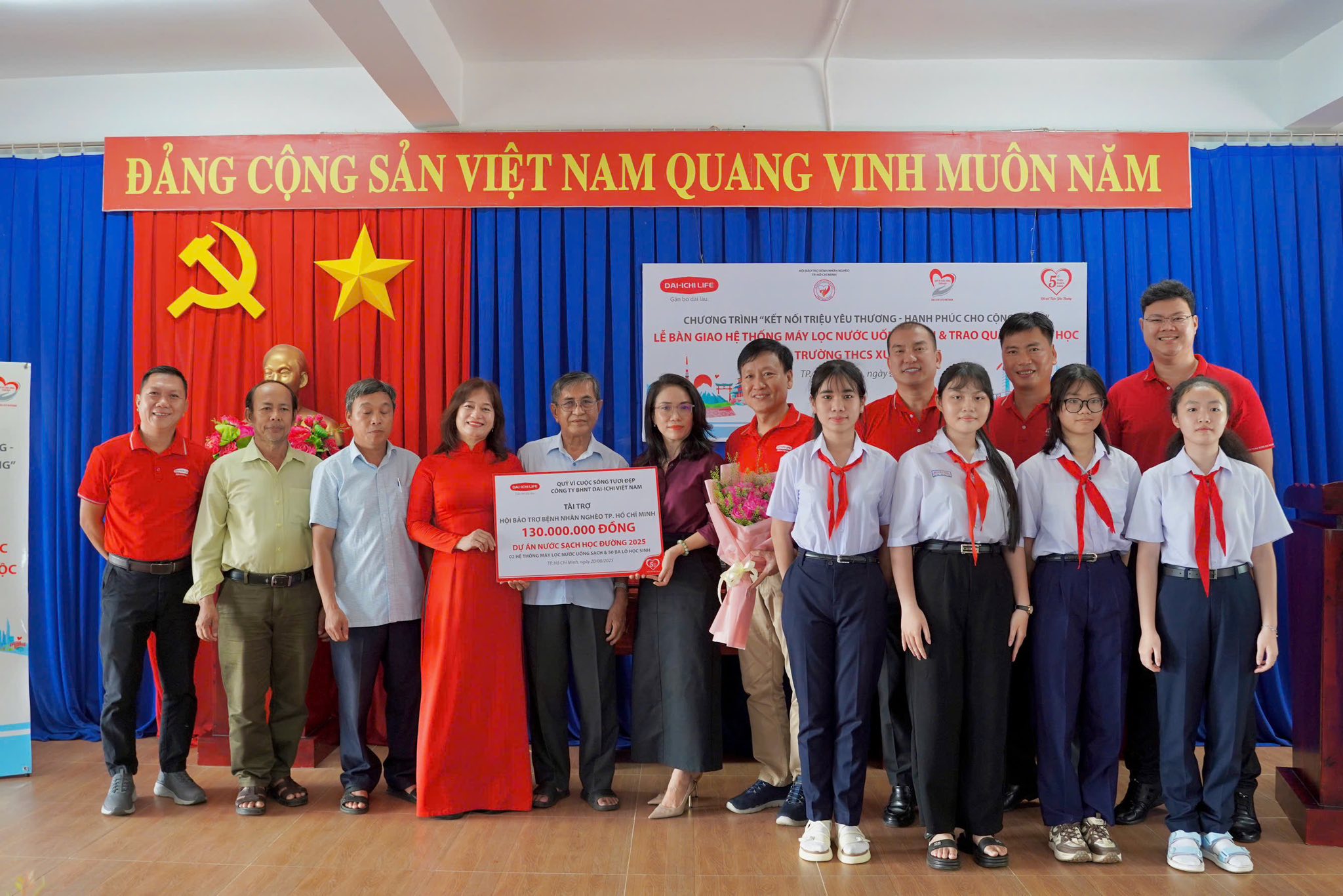 Ông Trần Đình Quân, Chủ tịch Hội đồng Thành viên Dai-ichi Life Việt Nam, kiêm Chủ tịch Quỹ Vì cuộc sống tươi đẹp (áo đỏ, thứ tư từ bên phải) trao biểu trưng tài trợ hệ thống máy lọc nước uống sạch và quà khuyến học cho Ban Giám hiệu Trường THCS Xuyên Mộc, Xã Xuyên Mộc, TP. Hồ Chí Minh